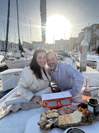 a man and woman sitting on a boat with food and wine