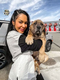 a woman holding a large dog in front of a car