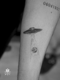 a black and white image of an ufo flying over a man's forearm
