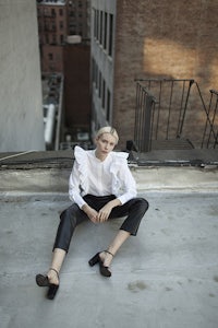 a woman sitting on the edge of a building wearing leather pants and a ruffled blouse