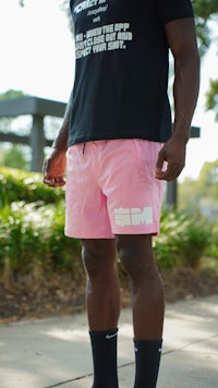 a man in pink shorts and black t - shirt standing on a sidewalk