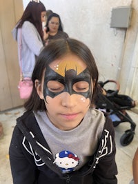 a little girl with a batman face painted on her face