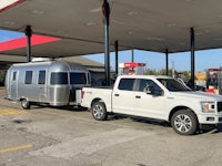 a white truck with an airstream trailer parked in front of a gas station