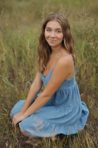 a girl in a blue dress sitting in a field