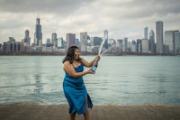 a woman is holding a bottle of champagne in front of the water with the chicago skyline in the background