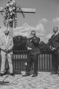 black and white photo of groom and groomsmen in front of a cross