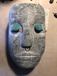 a stone head with turquoise eyes sitting on a table