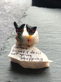two figurines sitting on a rock with a piece of paper