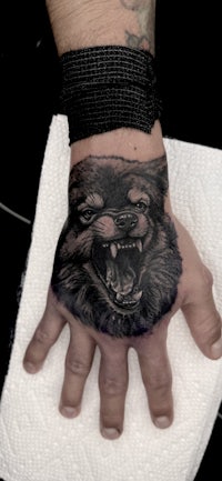 a black and white tattoo of a wolf on a man's hand