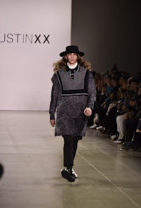 a model walks down the runway wearing a hat and sweater