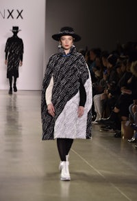 a model walks down the runway wearing a cape and hat