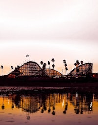 a roller coaster is reflected in the water at dusk