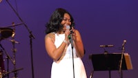 a woman in a white dress singing into a microphone