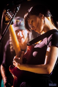 a woman playing an electric guitar in front of a man