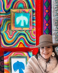 a woman wearing a hat and a hat in front of colorful paintings