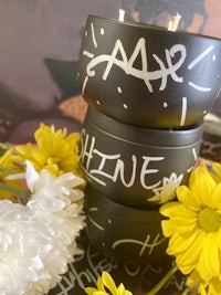 a stack of black candle jars with yellow flowers in them