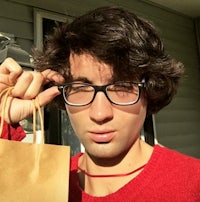 a young man with glasses holding a paper bag