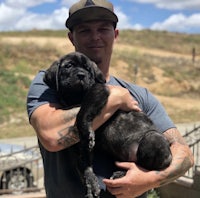 a man holding a black puppy in his arms