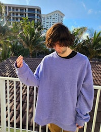 a man standing on a balcony wearing a purple sweatshirt