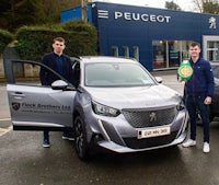 two men standing next to a peugeot car