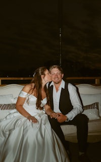 a bride and groom kissing on a couch at night