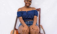 a young woman sitting on a chair next to an acoustic guitar
