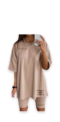 a woman is taking a selfie in a beige t - shirt and shorts