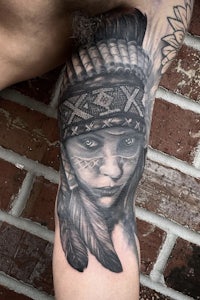 a tattoo of an indian woman with feathers on her arm