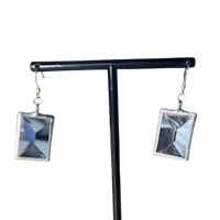 a pair of silver square earrings on a black stand
