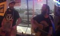 two men playing guitar and singing in a bar