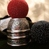 a black and red beaded ball sits on top of a silver cup