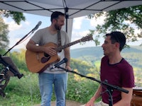 two men playing guitar and singing under a tent