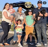 a family standing in front of a car with a dog in the trunk