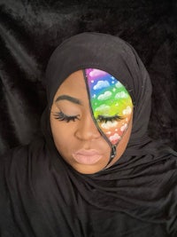 a woman wearing a black hijab with rainbow eye makeup