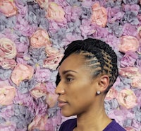 a woman in front of a flower wall with a braided hairstyle