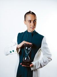 a woman in a white and green suit holding an hourglass