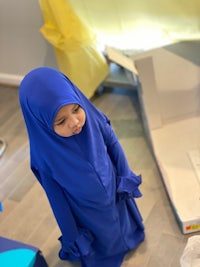 a little girl in a blue hijab standing in a room