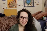 a woman in glasses smiling in front of a bed