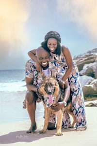a man and woman pose with their dog on the beach