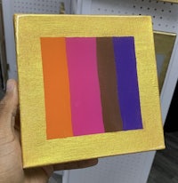 a person holding a yellow, orange, and purple painting in a box