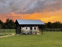 an airstream parked in a field with a sunset behind it