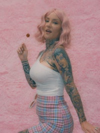a woman with pink hair and tattoos posing on a pink wall