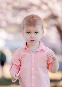 a young boy in a pink shirt standing in a park