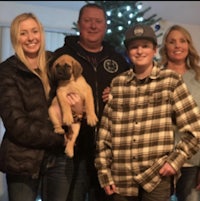 a family posing with a puppy in front of a christmas tree