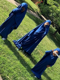 three children in blue robes standing in a grassy area