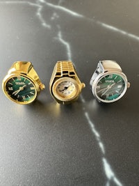 three gold and green watches on a table