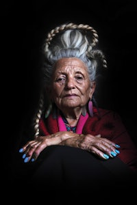 an old woman with braided hair sitting on a black background