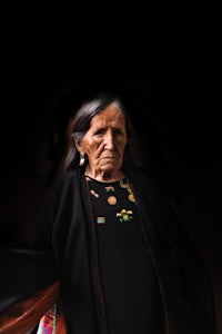 an old woman is standing in front of a dark background