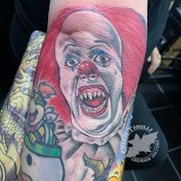a tattoo of a clown with teeth on his arm