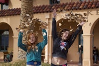two girls throwing leaves in front of a building
